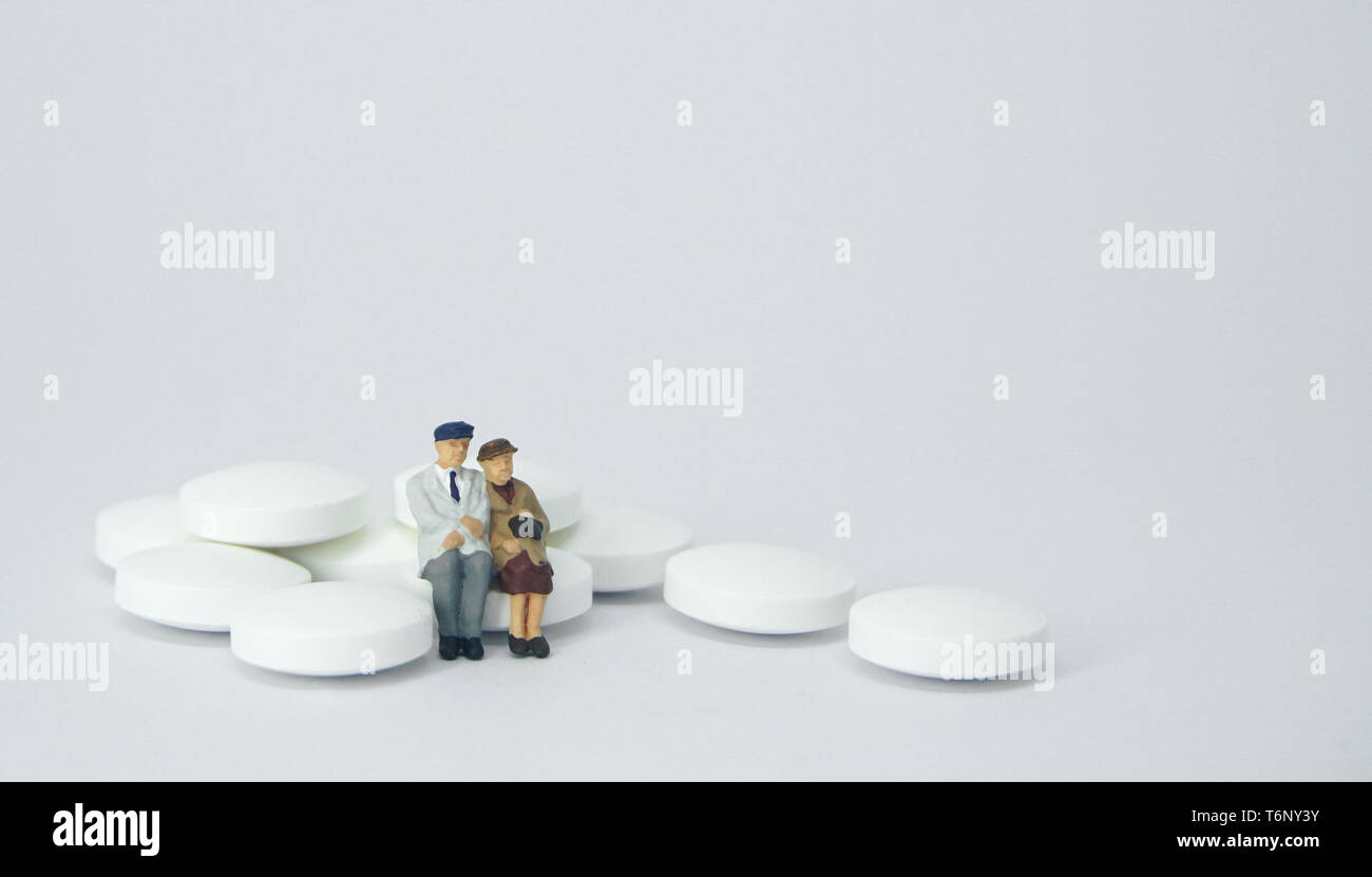 Coppia di anziani la figura seduta su una pila di pillole di bianco. Foto Stock