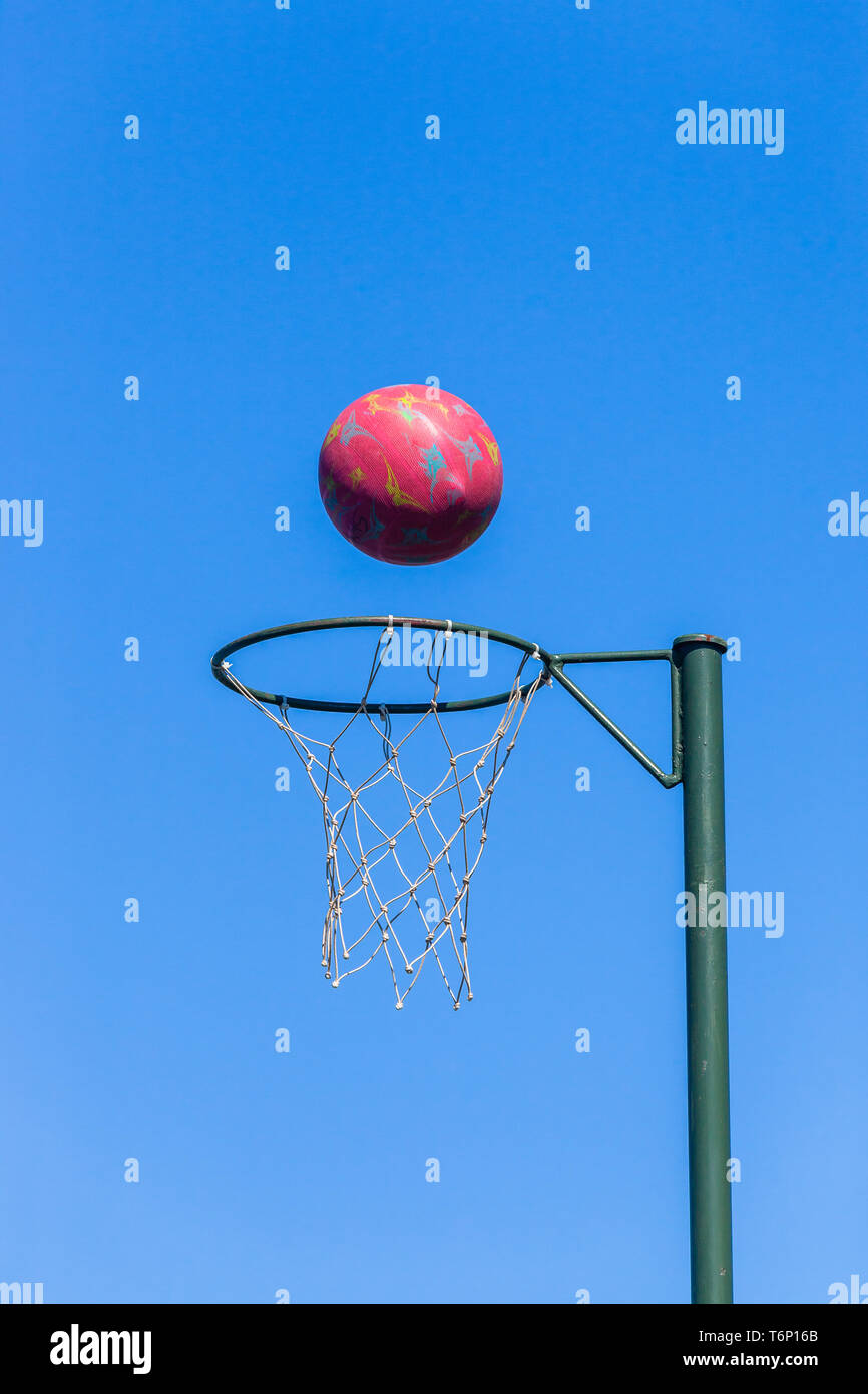 Netball hoop net con sfera rossa in volo contro il cielo blu . Foto Stock