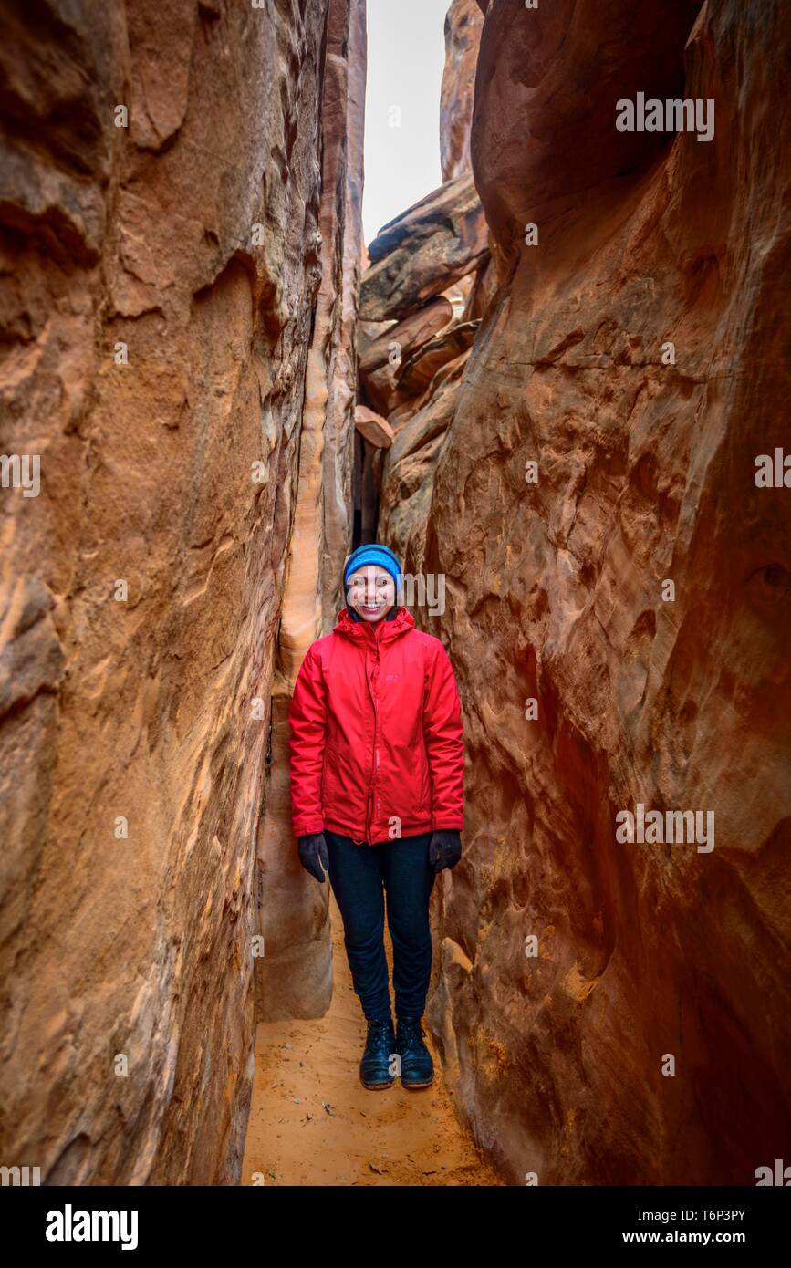Giovane donna in piedi di spazio tra le rocce, Dune di sabbia Arch, Arches National Park, vicino a Moab, Utah, Stati Uniti d'America Foto Stock