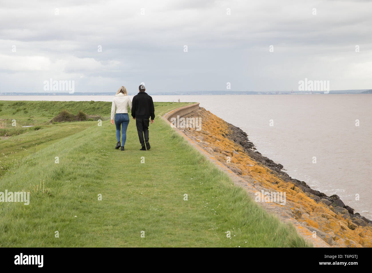 Goldcliff, Newport, Regno Unito. Il 2 maggio, 2019. La gente a piedi lungo la parete del mare nonostante un ventoso, grigio e triste giorno in Goldcliff, Newport, Galles. La parete del mare si affaccia sul fiume Severn offrendo fantastiche vedute attraverso l'acqua. Credito: Keith Larby/Alamy Live News Foto Stock