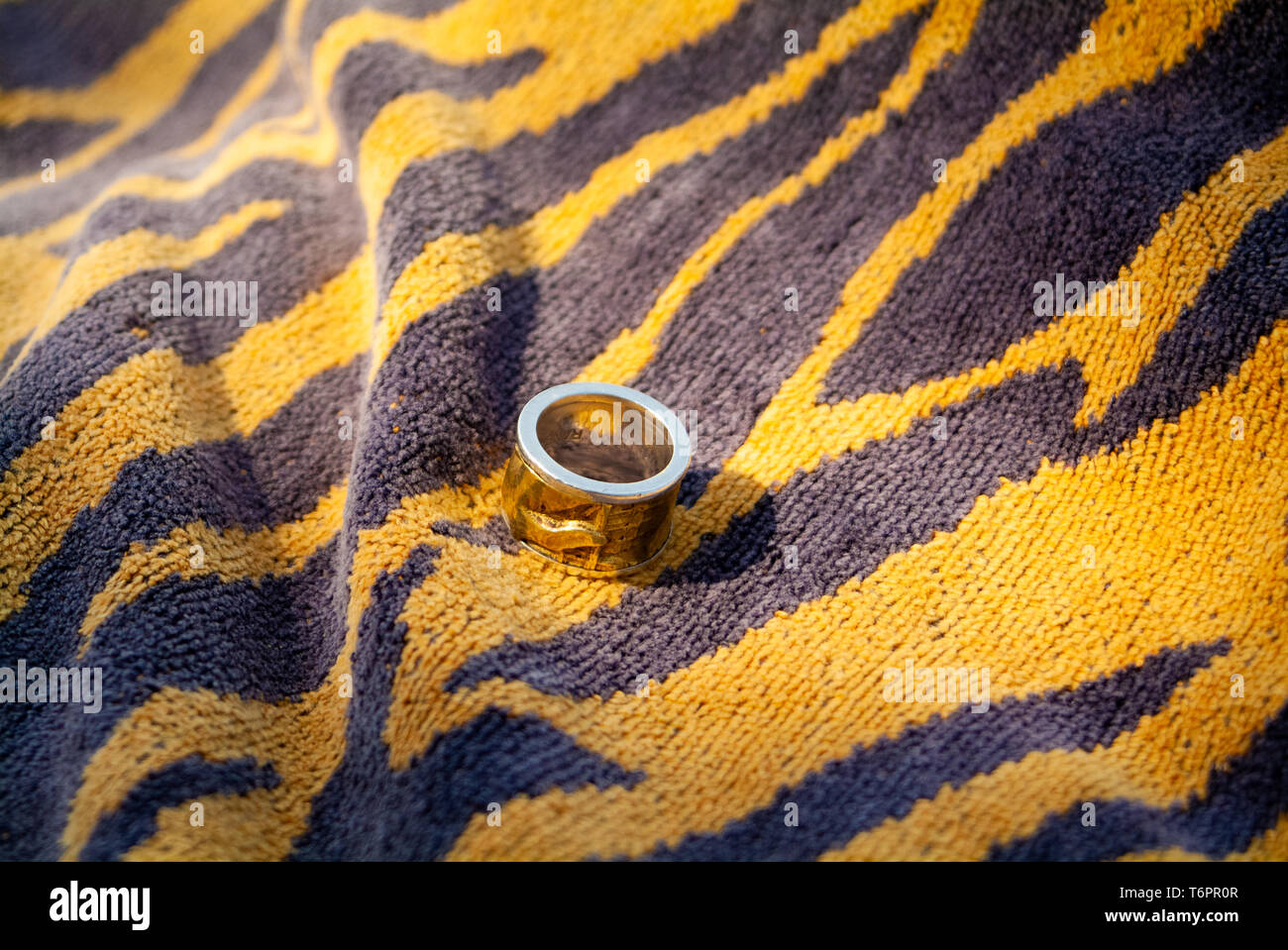 Versione maschio di un matrimonio Bronze e Silver Ring sulla spiaggia di giallo e nero asciugamano Foto Stock