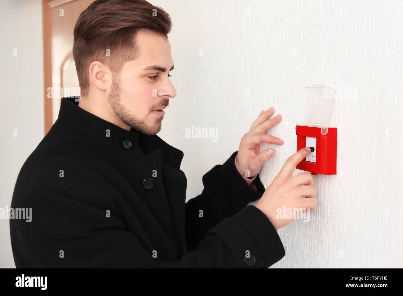 Giovane uomo spingendo il pulsante del sistema di allarme antincendio, in interni Foto Stock