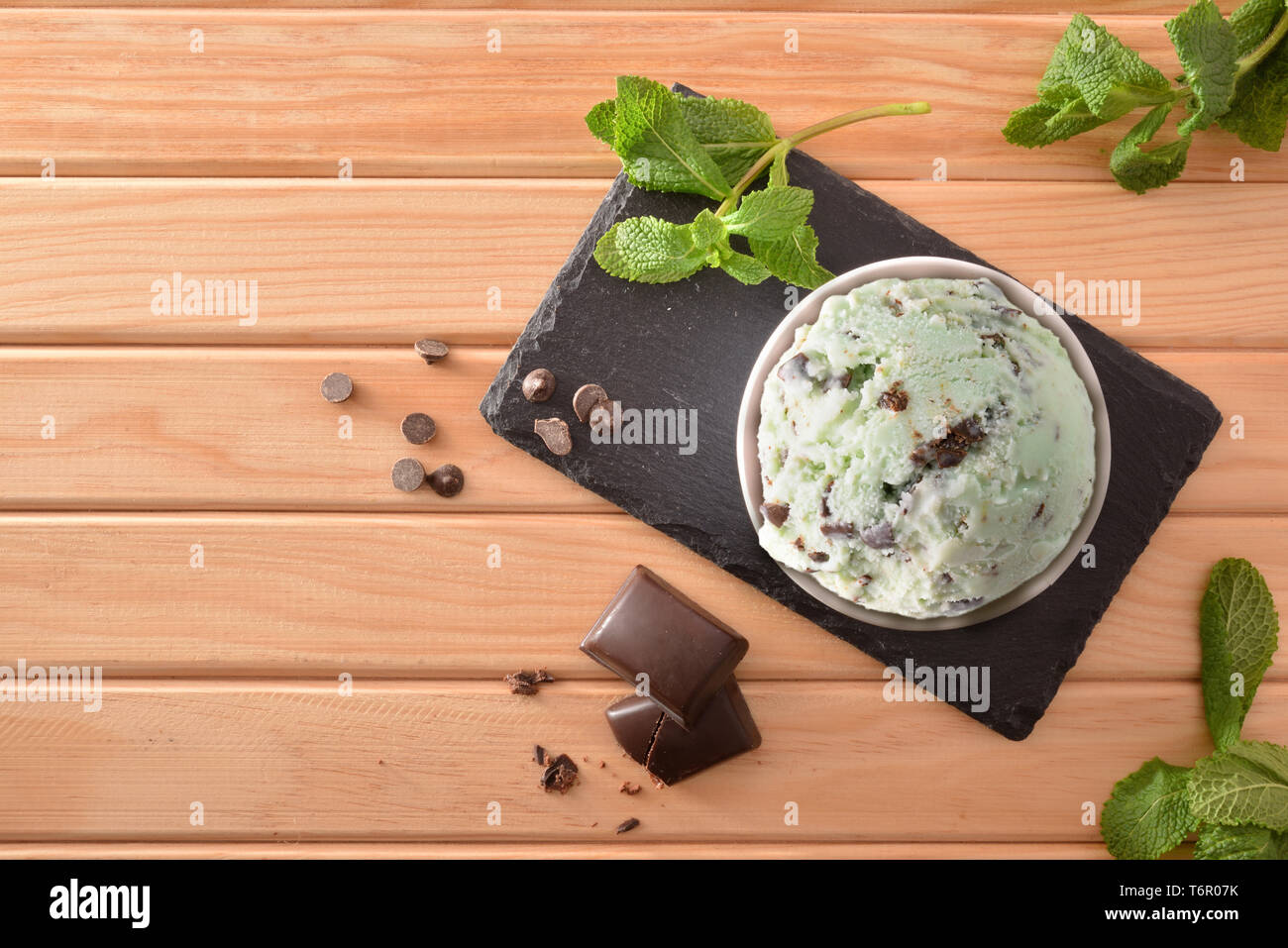 La menta e choco coppa di gelato decorato con foglie di menta e scaglie di cioccolato sul piatto di ardesia su un tavolo di legno. Composizione orizzontale. Vista dall'alto. Foto Stock