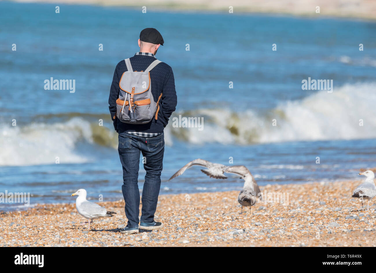 Uomo che cammina da sola portando uno zaino su una spiaggia in primavera nel Regno Unito. Foto Stock