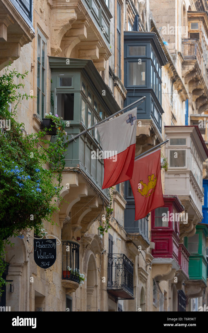Bandiere volare da tradizionali case di maltese in St Paul Street con la loro vibrante, racchiusi in legno balconi (galleriji) e facciate di pietra calcarea Foto Stock
