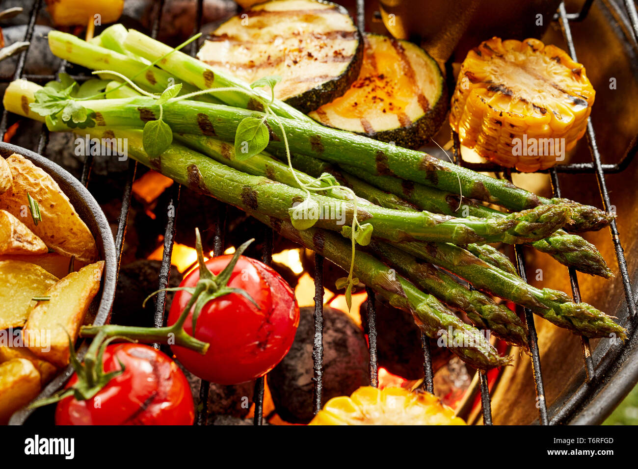 Una sana verdura fresca la cottura alla griglia su un barbecue con zucchine, Spicchi di patate asparagi, pomodoro e sulla pannocchia di mais in una vista ravvicinata Foto Stock