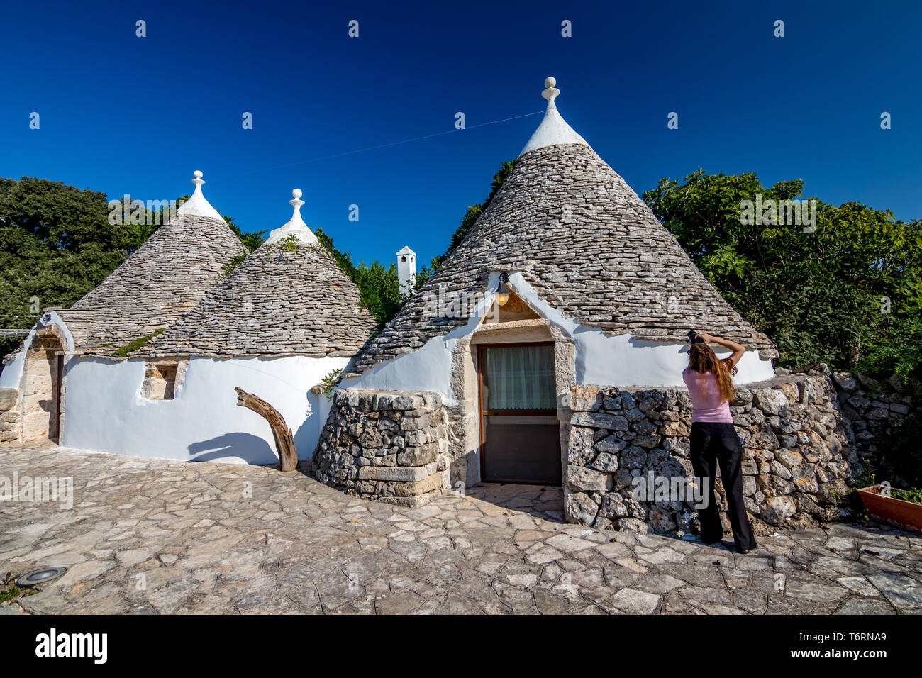 GIOIA DEL COLLE, Italia - 28 agosto 2018 - bella femmina irriconoscibile fotografo prende le foto di fronte all antica truli in chiaro blu-sky calda mattina d'estate. Regione Puglia, Italia Meridionale Foto Stock