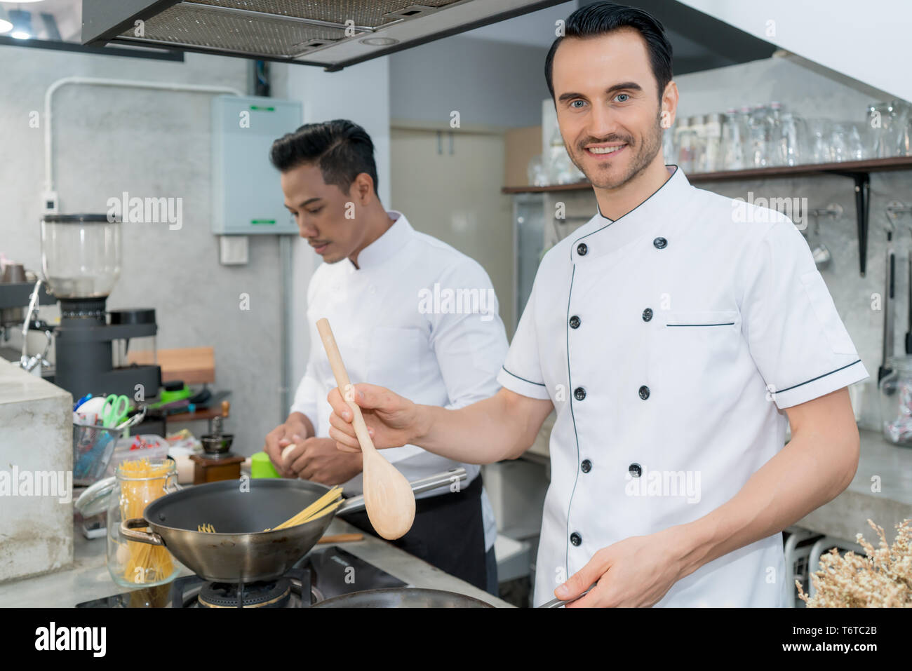 Ritratto di giovane maschio chef preparare spaghetti con il collega in cucina. Foto Stock