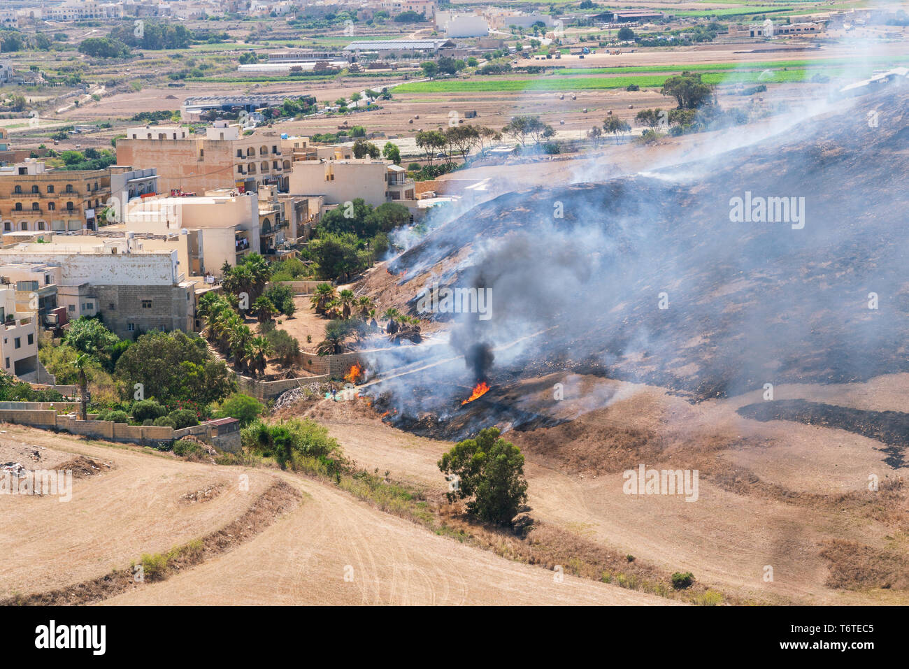 Fuoco d'erba in una calda giornata estiva nei pressi di abitazioni locali in Isola di Gozo, Malta. Foto Stock