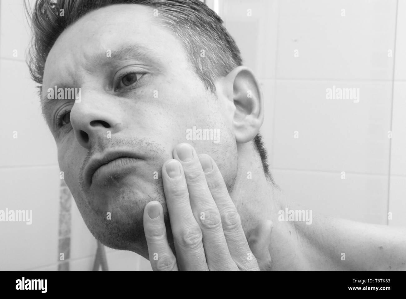 Uomo che guarda in uno specchio e applicazione del prodotto per la pelle sulla faccia in bagno Foto Stock