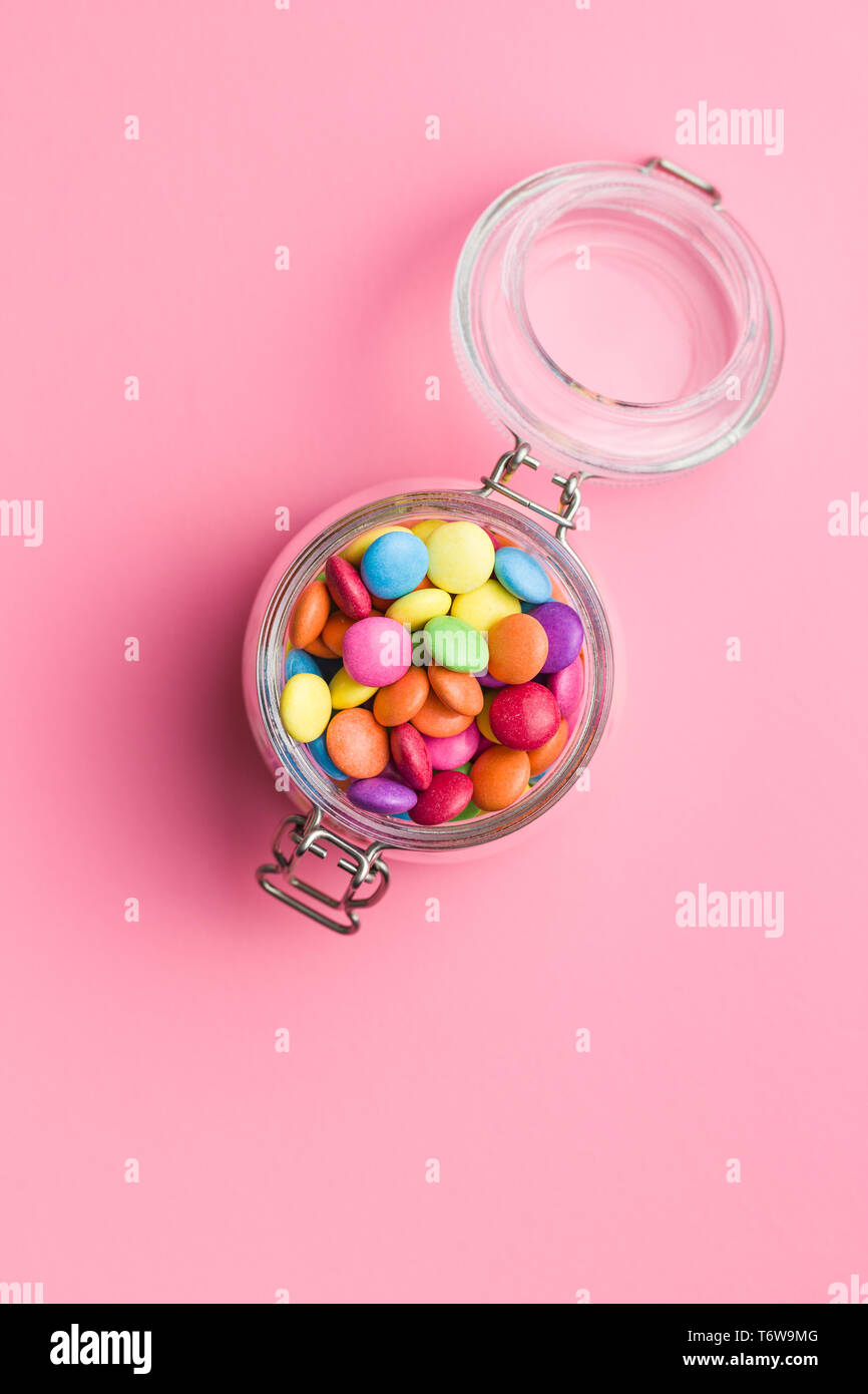 Cioccolato colorato candy pillole in vaso su sfondo rosa. Foto Stock