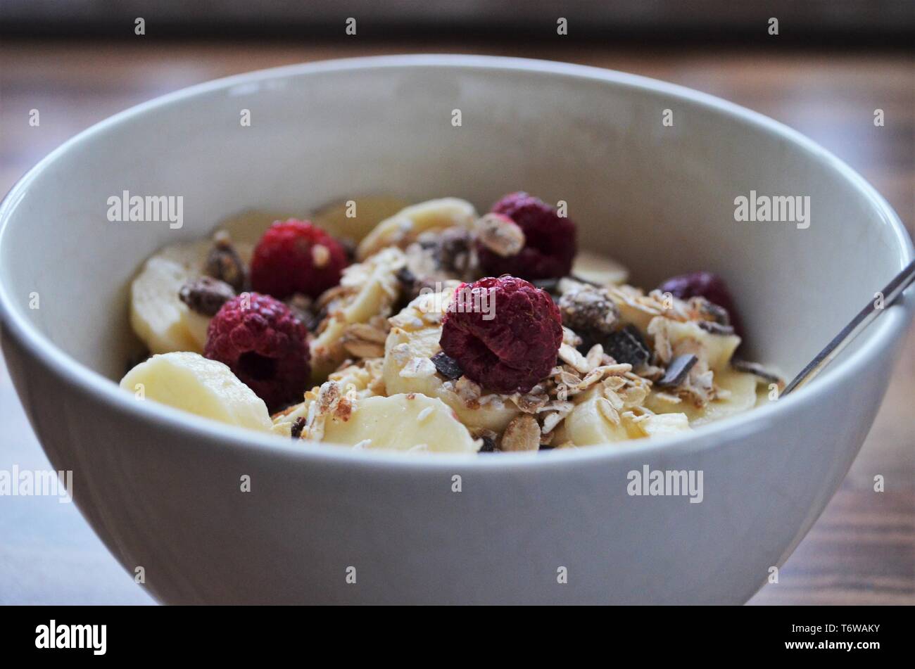 Buona la colazione mattutina, cereali in una ciotola con le banane e lamponi Foto Stock