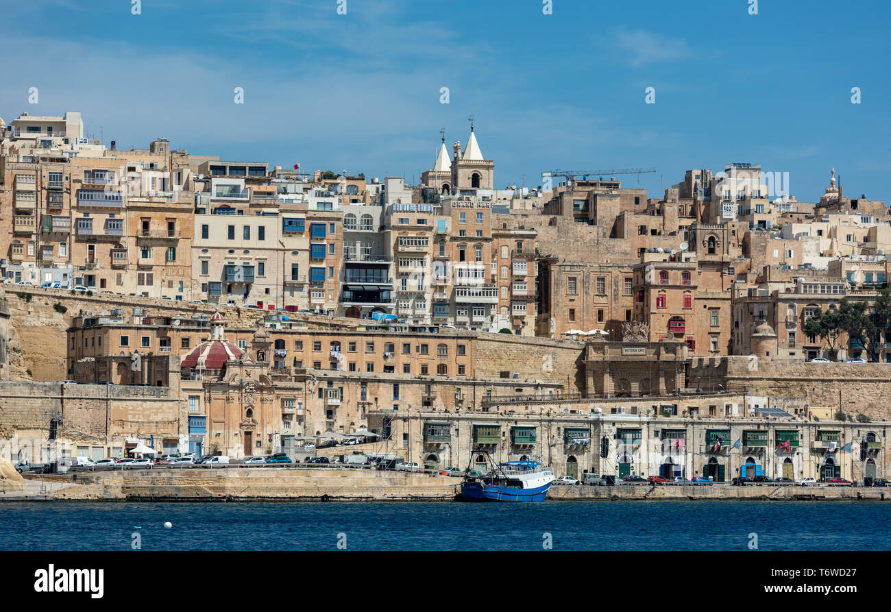 I bastioni e gli edifici storici in pietra calcarea fiancheggiano il lungomare di la Valletta e si affacciano su un blu profondo del Grand Harbour Foto Stock