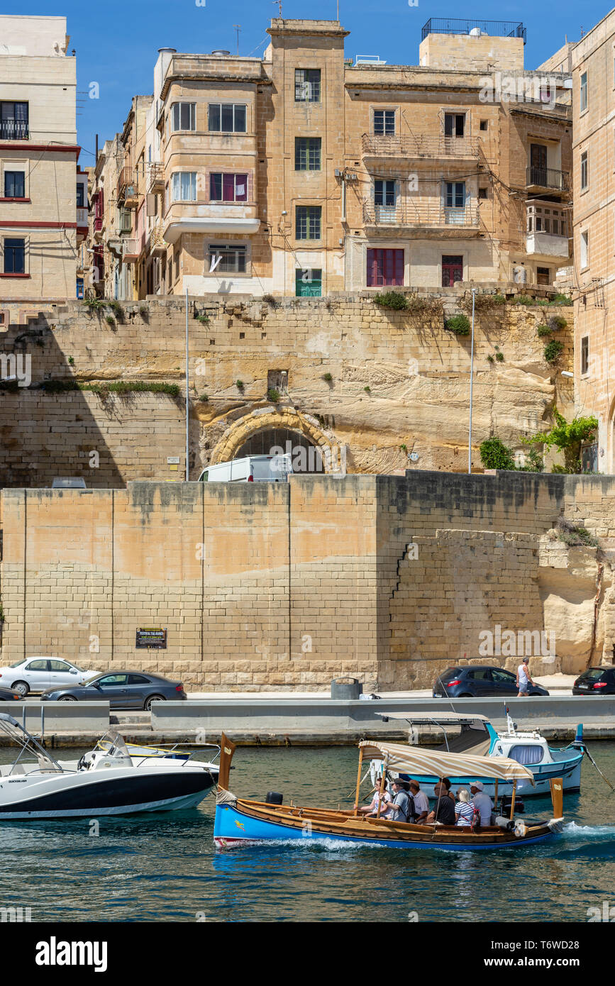 Dghajsa tal-Pass, il tradizionale taxi d'acqua maltese ferry turisti oltre gli storici edifici calcarei del lungomare di Senglea Foto Stock