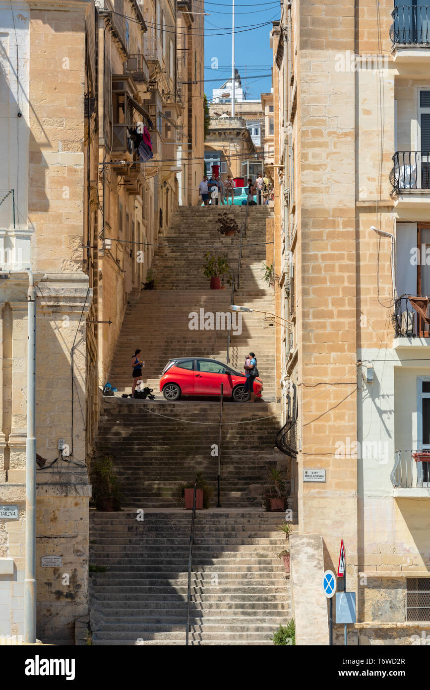 Una piccola auto rossa si trova sul Triq San Lawrenz, una stretta scalinata che porta da Xatt Juan B Azopardo sul lungomare di Senglea. Foto Stock