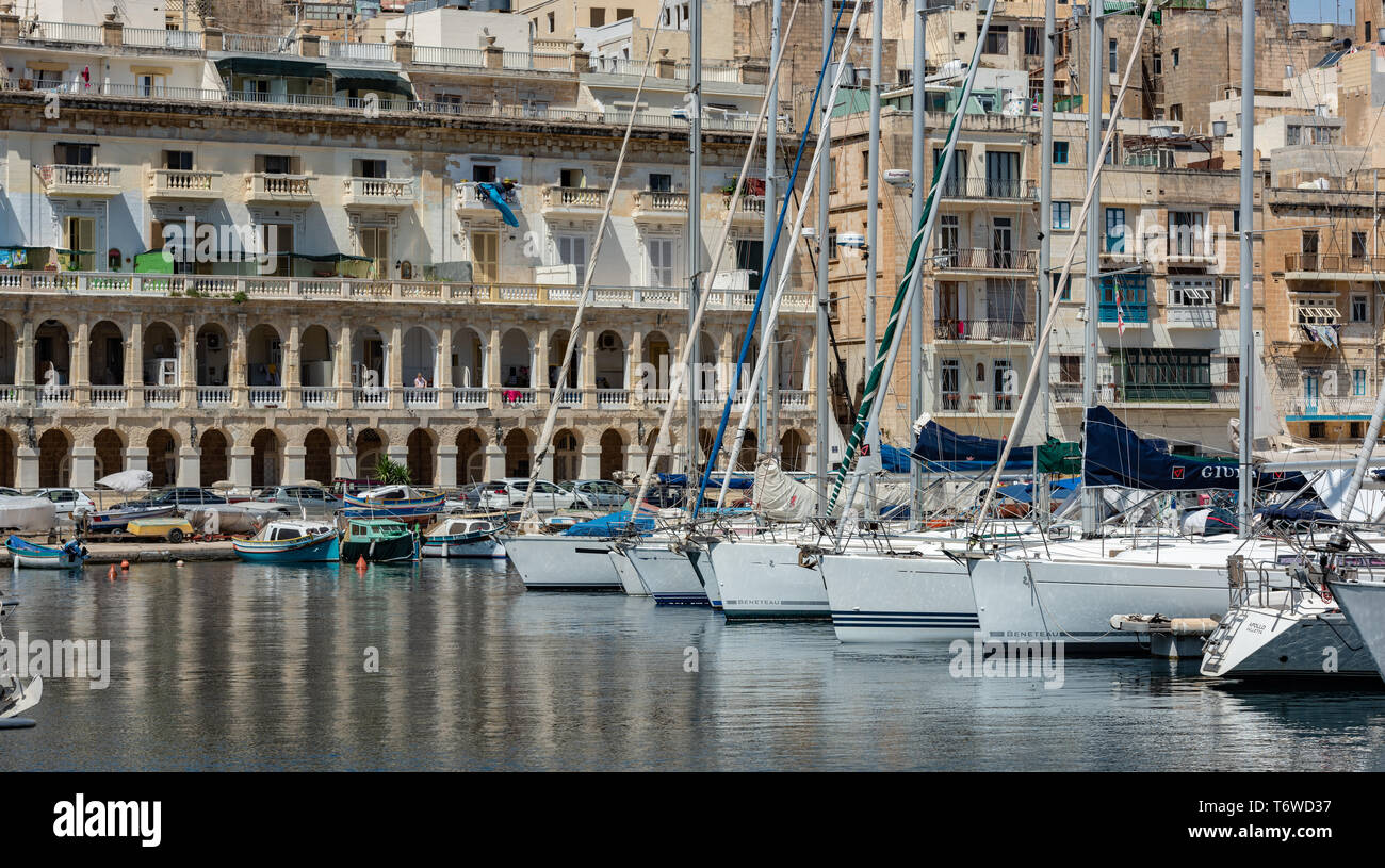 Barche a motore bianche e imbarcazioni da diporto nel Grand Harbour Marina di Vittoriosa, con gli storici edifici calcarei di Senglea che costeggiano il lungomare Foto Stock