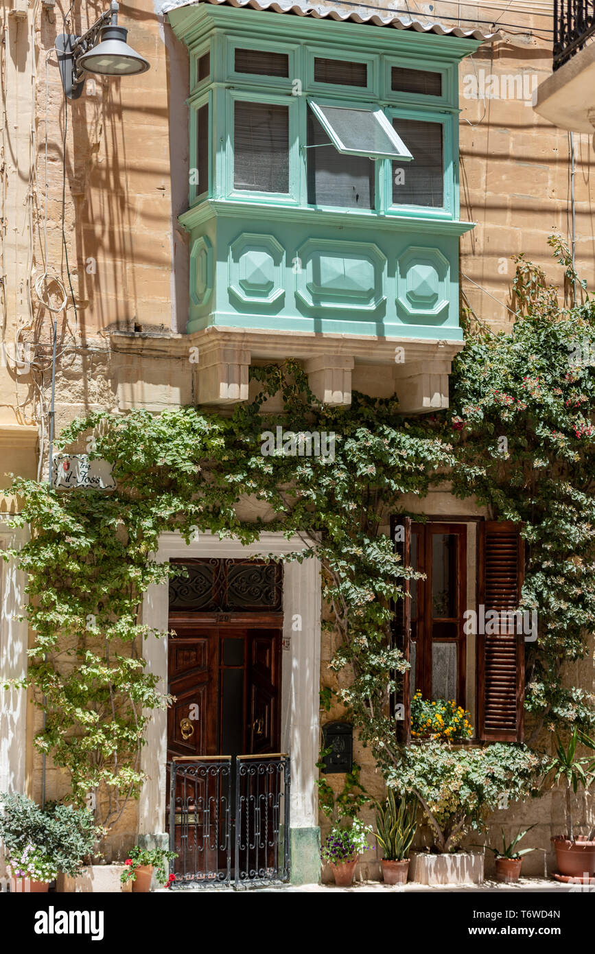 Una casa pittoresca a il-Birgu con il suo tradizionale balcone recintato in legno Gallarija e vegetazione verdeggiante intorno alla sua porta d'ingresso Foto Stock