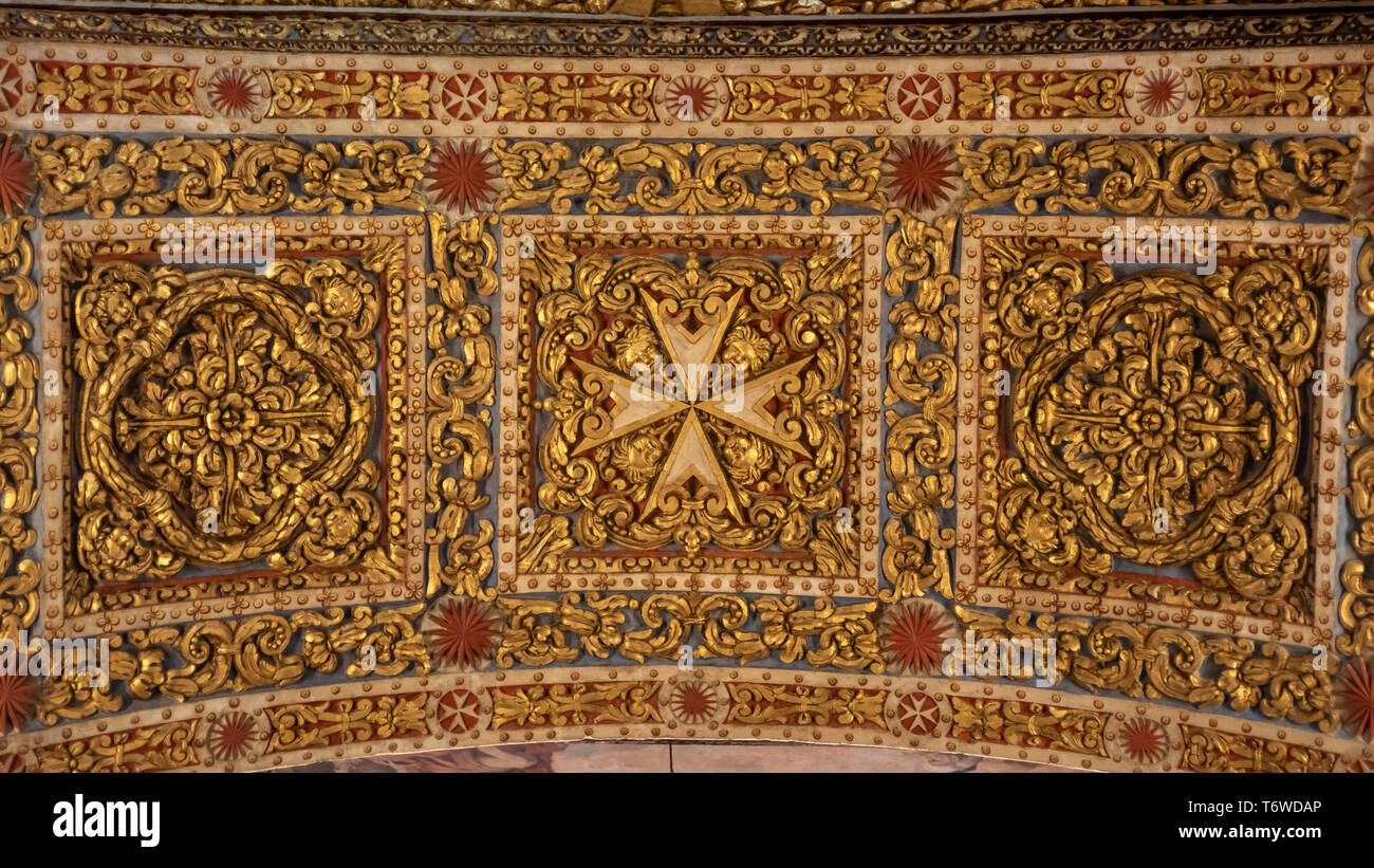 La croce maltese, decorata e intricatemente intagliata, e le rosette gemelle scolpite nella parte superiore di un arco nella co-cattedrale di San Giovanni a la Valletta, Foto Stock