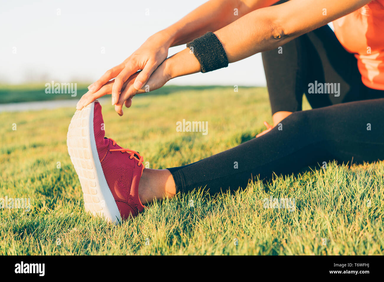 Giovani runner donna gambe stretching prima di correre in un parco. Close up atletico e sana bambina indossa bianco e rosa sneakers. Foto Stock