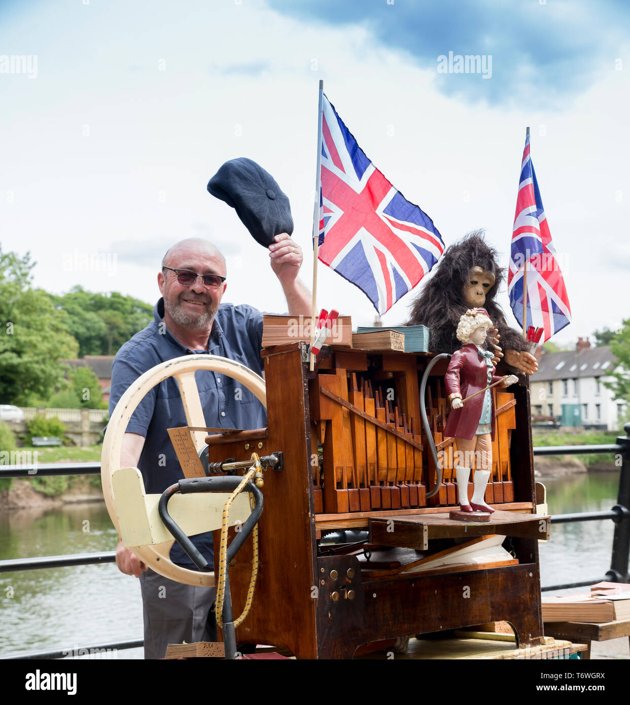 Uomini strada intrattenitore busking in città Worcestershire dal fiume per i turisti, giocando organo meccanico in strada pubblica, Regno Unito. Berretto uomo che doffing. Foto Stock