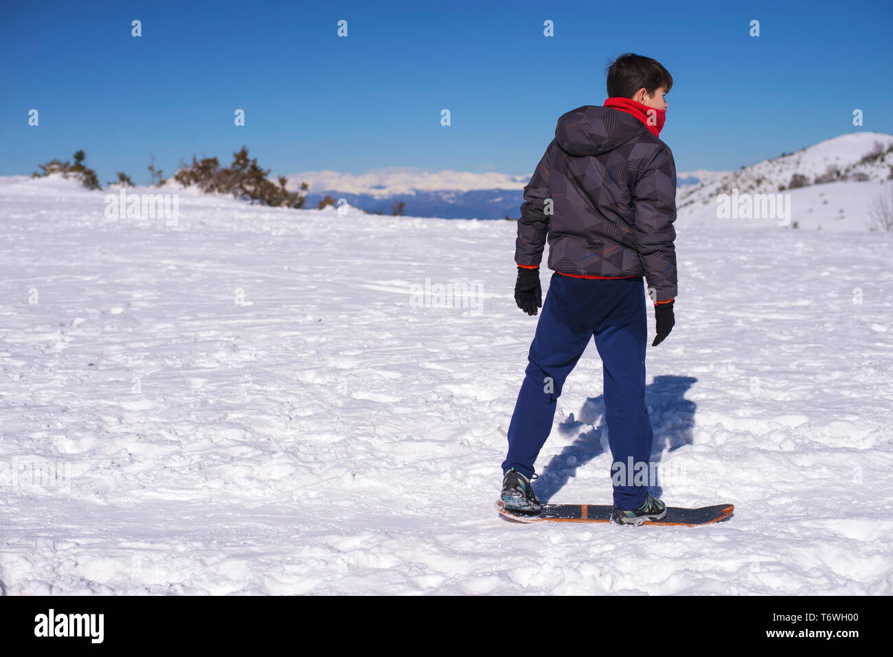 Vista laterale del giovane ragazzo lo snowboard sulla neve coperto hill nella giornata di sole Foto Stock