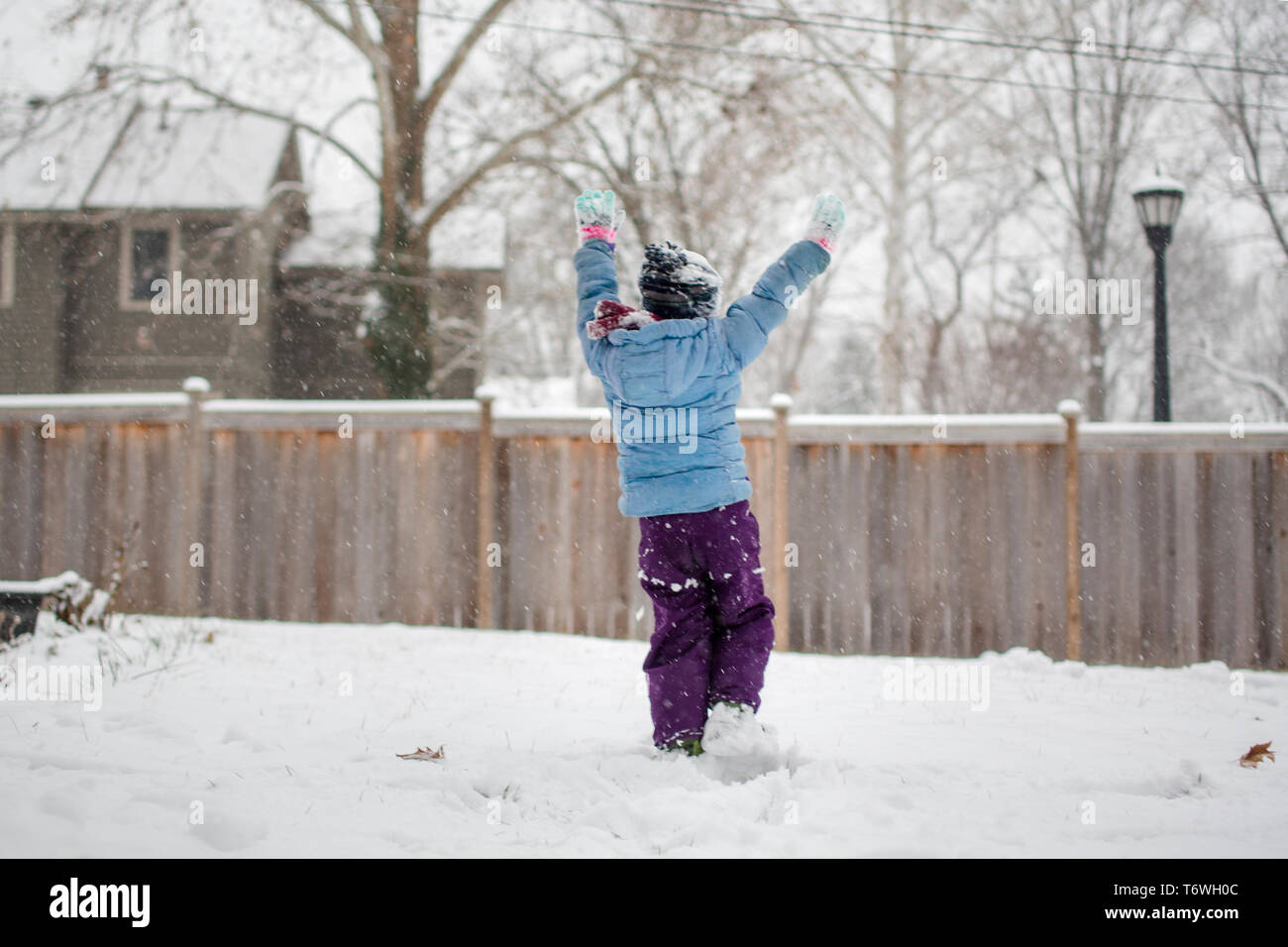 Un gioioso bambino alza braccia al cielo e gioca nella neve Foto Stock