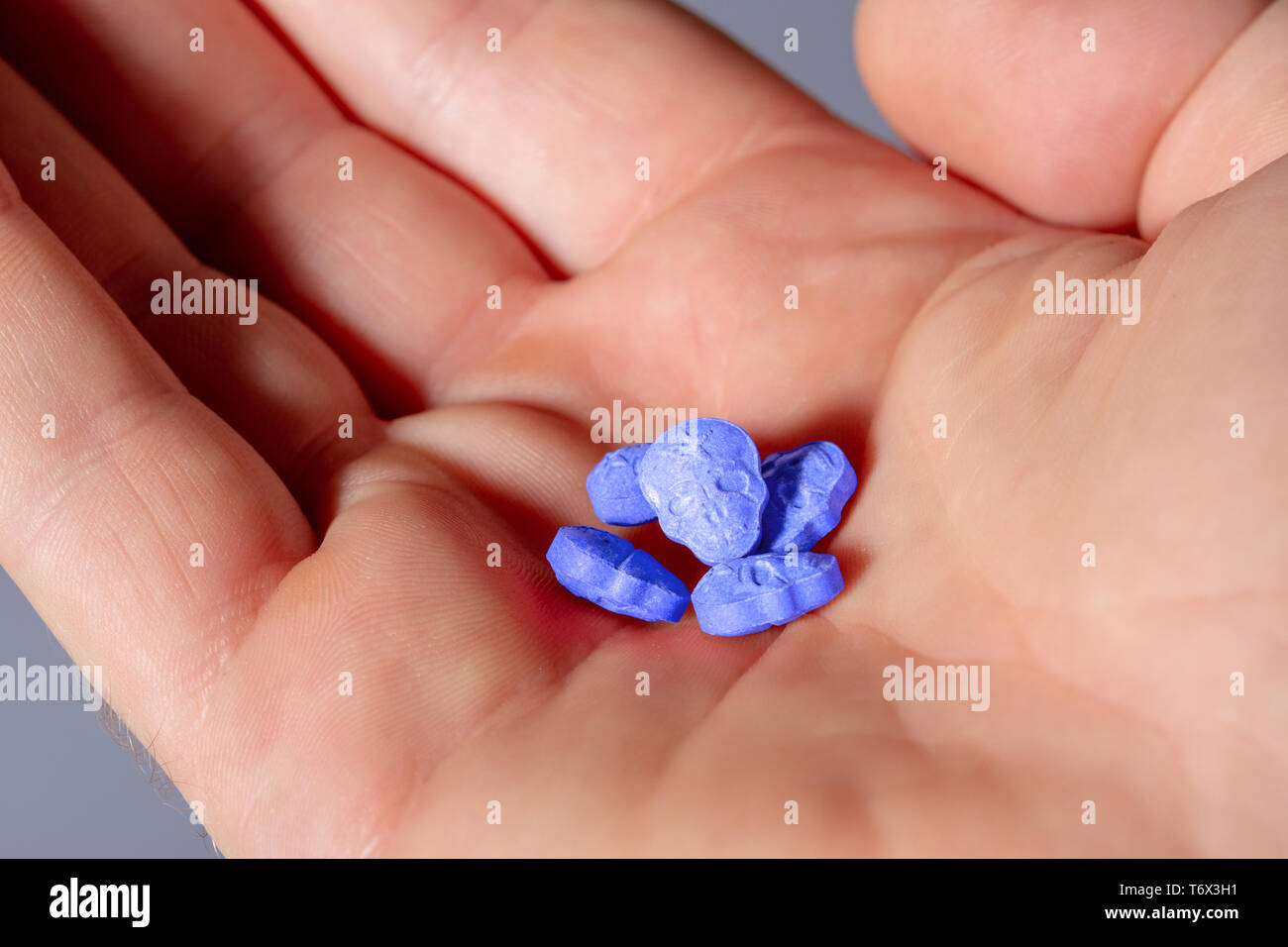 Un open caucasica mano maschio con un po' di pila di Esercito Blu cranio, ecstasy, MDMA, anfetamine o farmaco pillole conformata come un teschio sul. Foto Stock