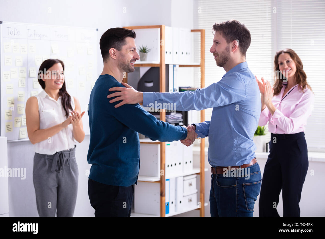 Due partner felice agitando mani mentre altri colleghi battimani in Office Foto Stock