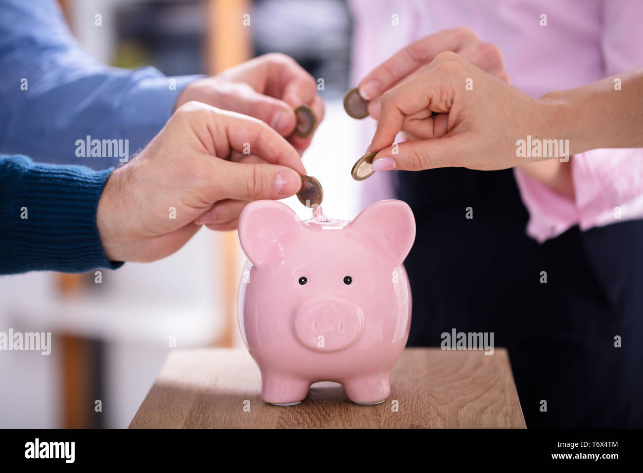 Gli imprenditori di mano inserire monete in rosa Piggybank in Office Foto Stock
