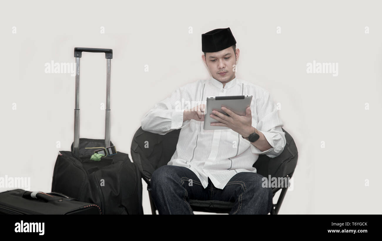 Ritratto di bello musulmani asiatici uomo con cappuccio di testa seduto sul divano con la valigia di bagagli e utilizzando la scheda ticket di ordinazione per il ramadan eid mubarak Foto Stock