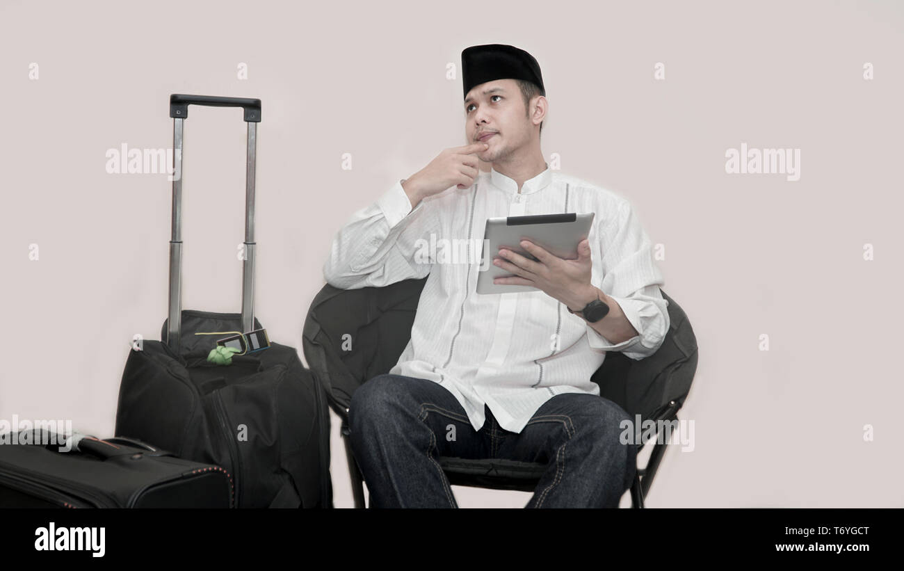 Ritratto di bello musulmani asiatici uomo con cappuccio di testa seduto sul divano con la valigia di bagagli e utilizzando la scheda ticket di ordinazione per il ramadan eid mubarak Foto Stock