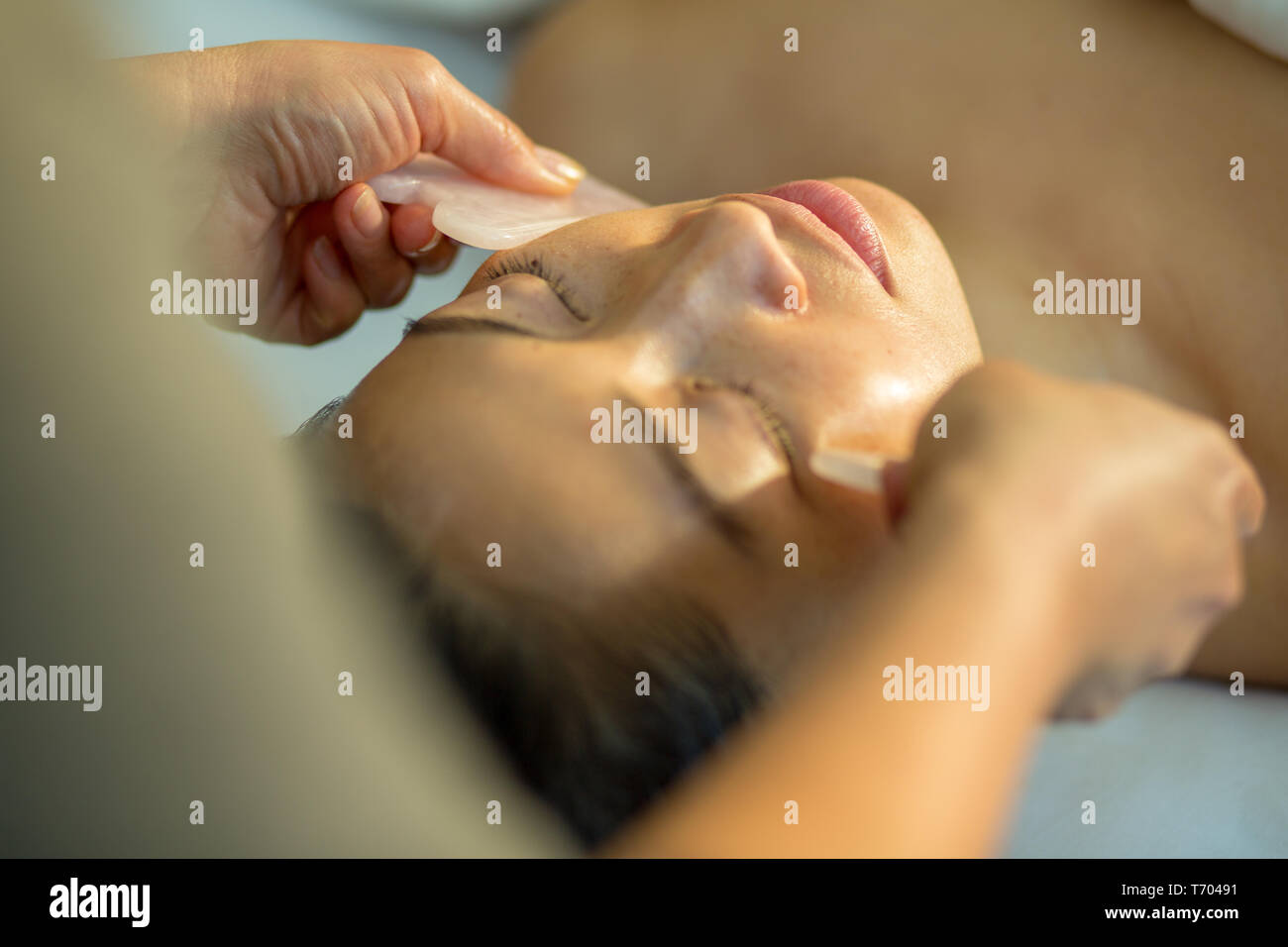 Giovane donna ricezione di ringiovanimento del viso gua sha raschiando il trattamento con quarzo rosa in agopuntura wellness spa clinica Foto Stock
