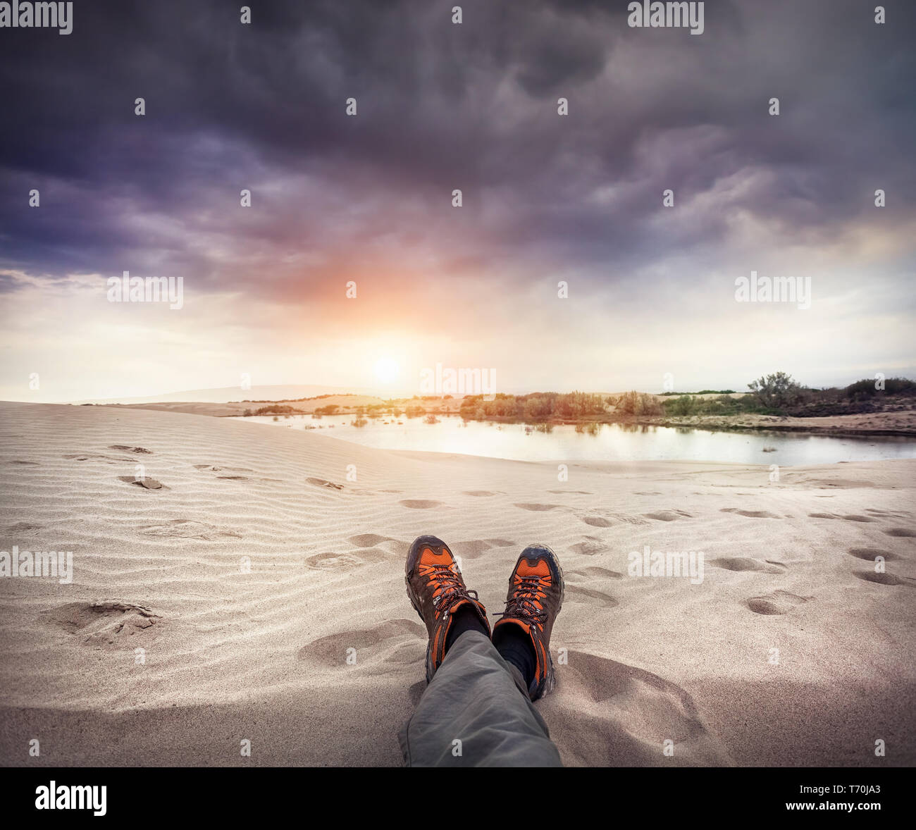 Gambe con arancione scarpe sulla duna di sabbia al tramonto sfondo con cielo nuvoloso Foto Stock