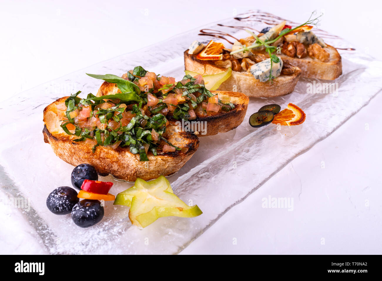 Stuzzicanti pomodoro antipasti italiani o bruschetta, su fette di pane abbrustolito baguette guarnita con basilico, close-up su uno sfondo bianco. Foto Stock