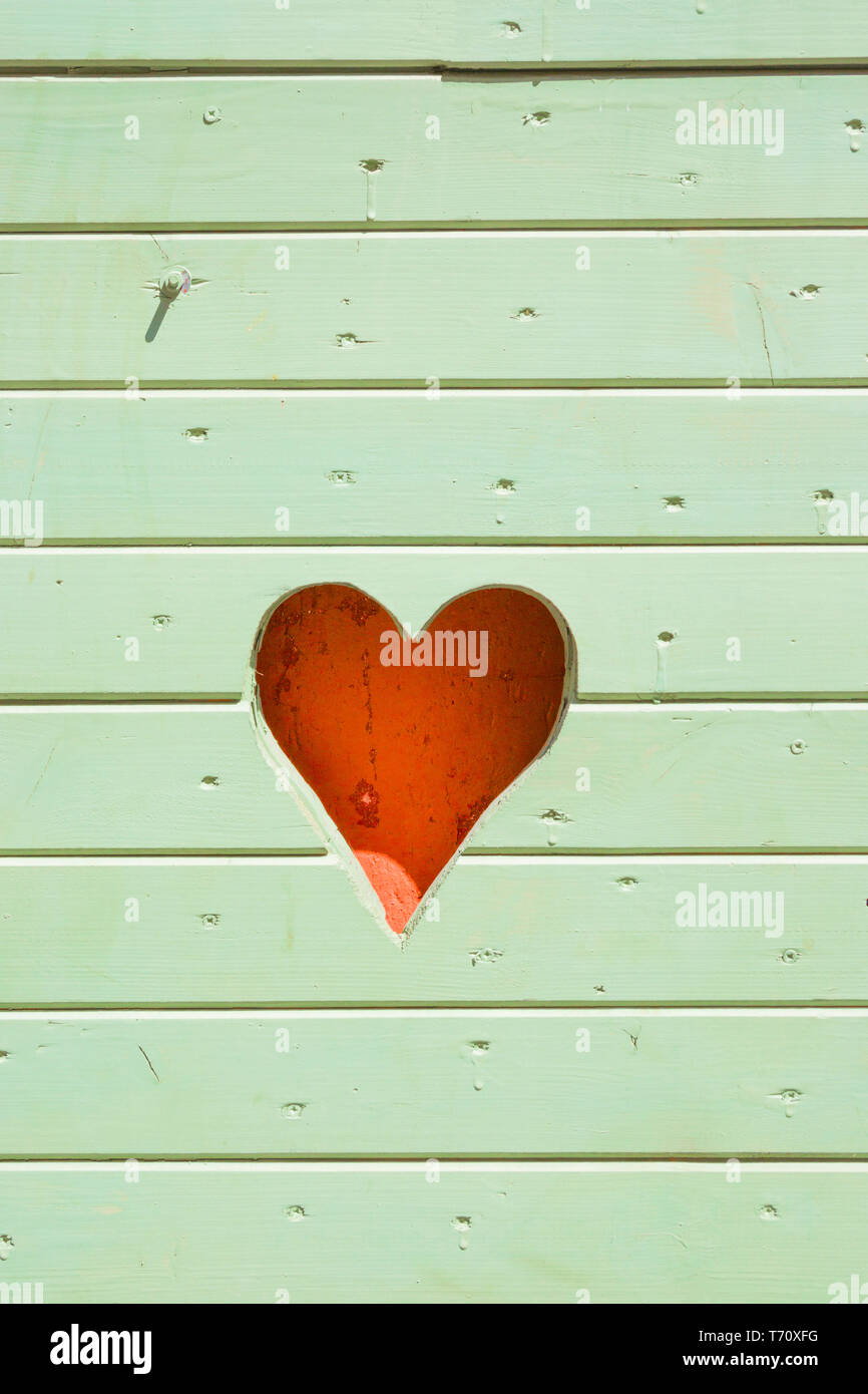 Cuore rosa tagliato a lato di una luce di legno verde beach hut Foto Stock