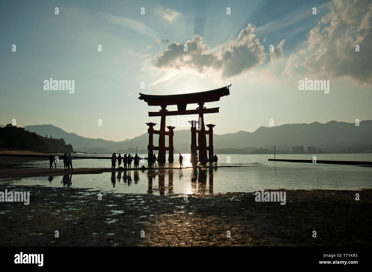Persone stagliano al tramonto accanto al giant floating torii gate del santuario di Itsukushima, l'isola di Miyajima, Western Honshu, Giappone, Asia Foto Stock