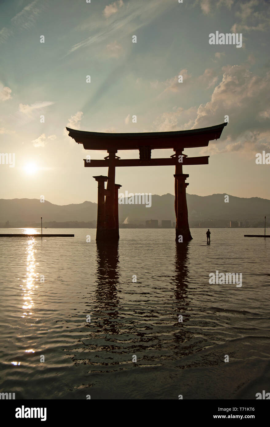 Persone stagliano al tramonto accanto al giant floating torii gate del santuario di Itsukushima, l'isola di Miyajima, Western Honshu, Giappone, Asia Foto Stock