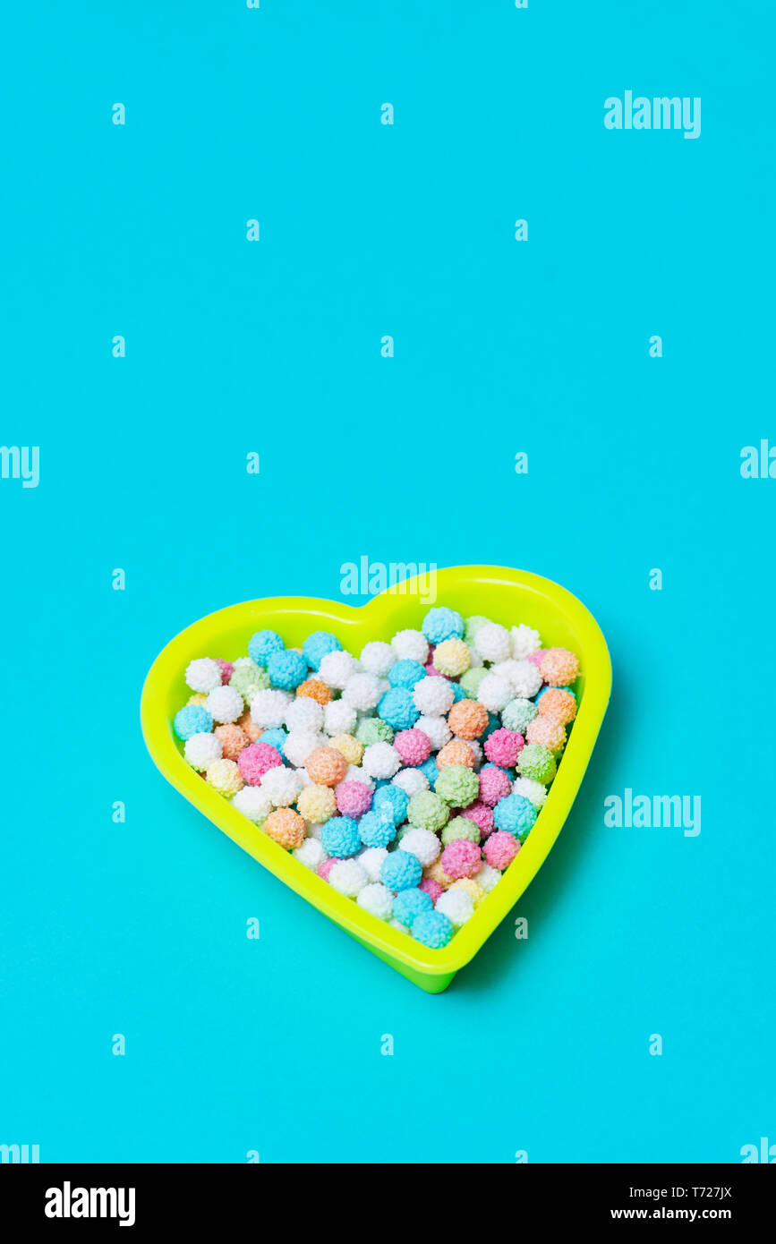 Un giallo in plastica a forma di cuore contenitore pieno di caramelle di colori differenti su uno sfondo blu, con uno spazio vuoto sulla parte superiore Foto Stock