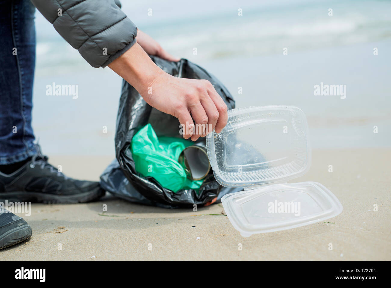 Primo piano di un uomo caucasico raccogliere rifiuti su una solitaria spiaggia, accanto all'acqua, come un intervento per pulire l'ambiente naturale Foto Stock