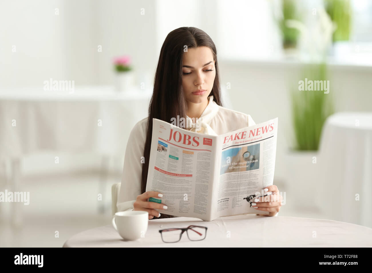 Giovane donna leggendo il giornale in cafe Foto Stock