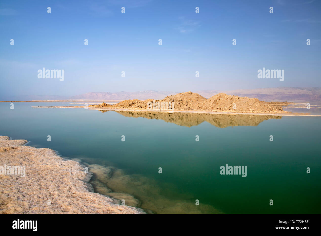 La riflessione di colline in acqua salata del Mar Morto sotto il quale sale formazioni sono visibili Foto Stock