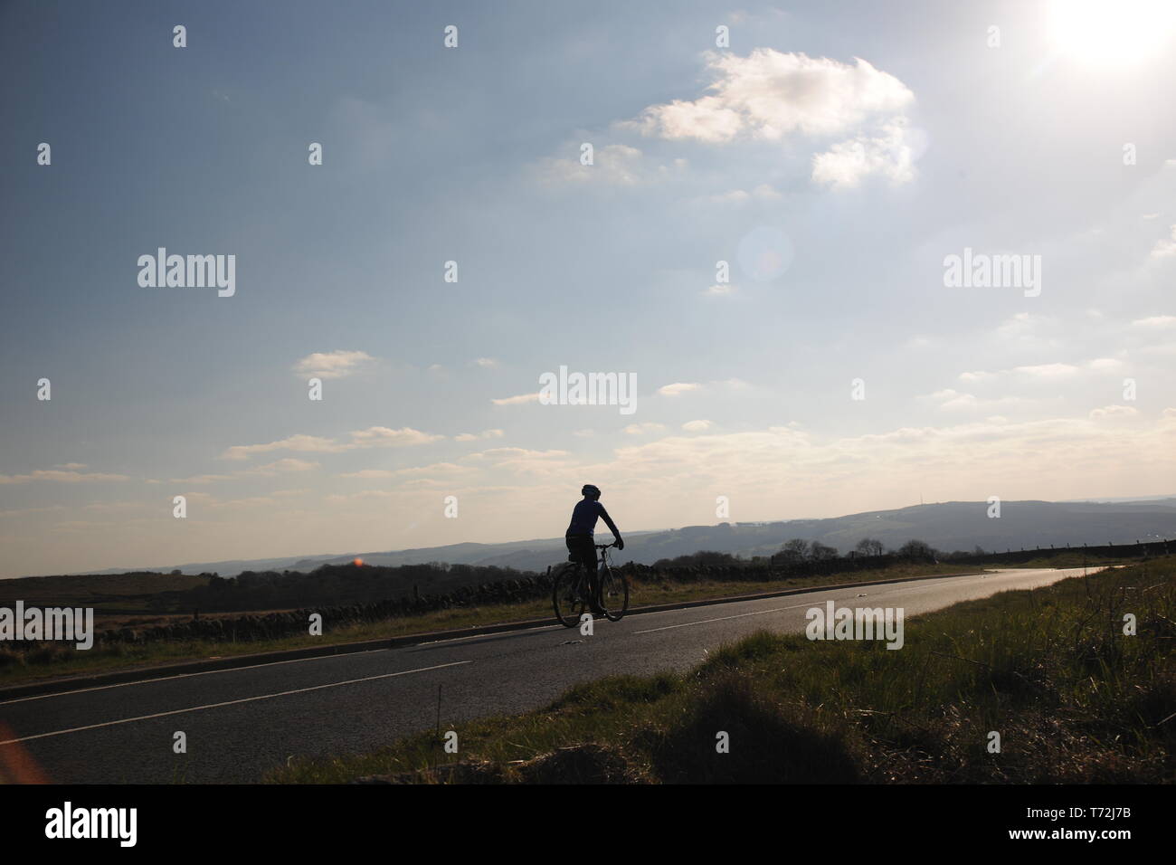 Ciclista a cavallo, lungo una strada di campagna nel distretto di Peak, con colline in lontananza Foto Stock