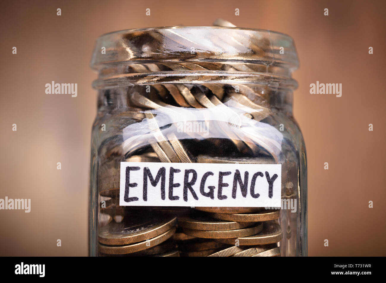 Monete in vaso con etichetta di emergenza sulla scrivania in legno Foto Stock