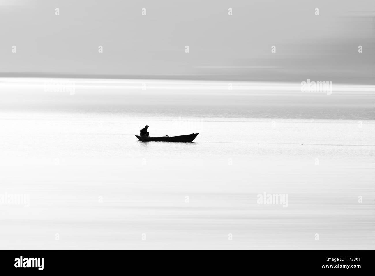 Un uomo si siede sulla barca e mettere Tutina in rete nel lago per pescare pesci di isolato grigio e sfondo bianco nel lago Phewa Nepal Foto Stock