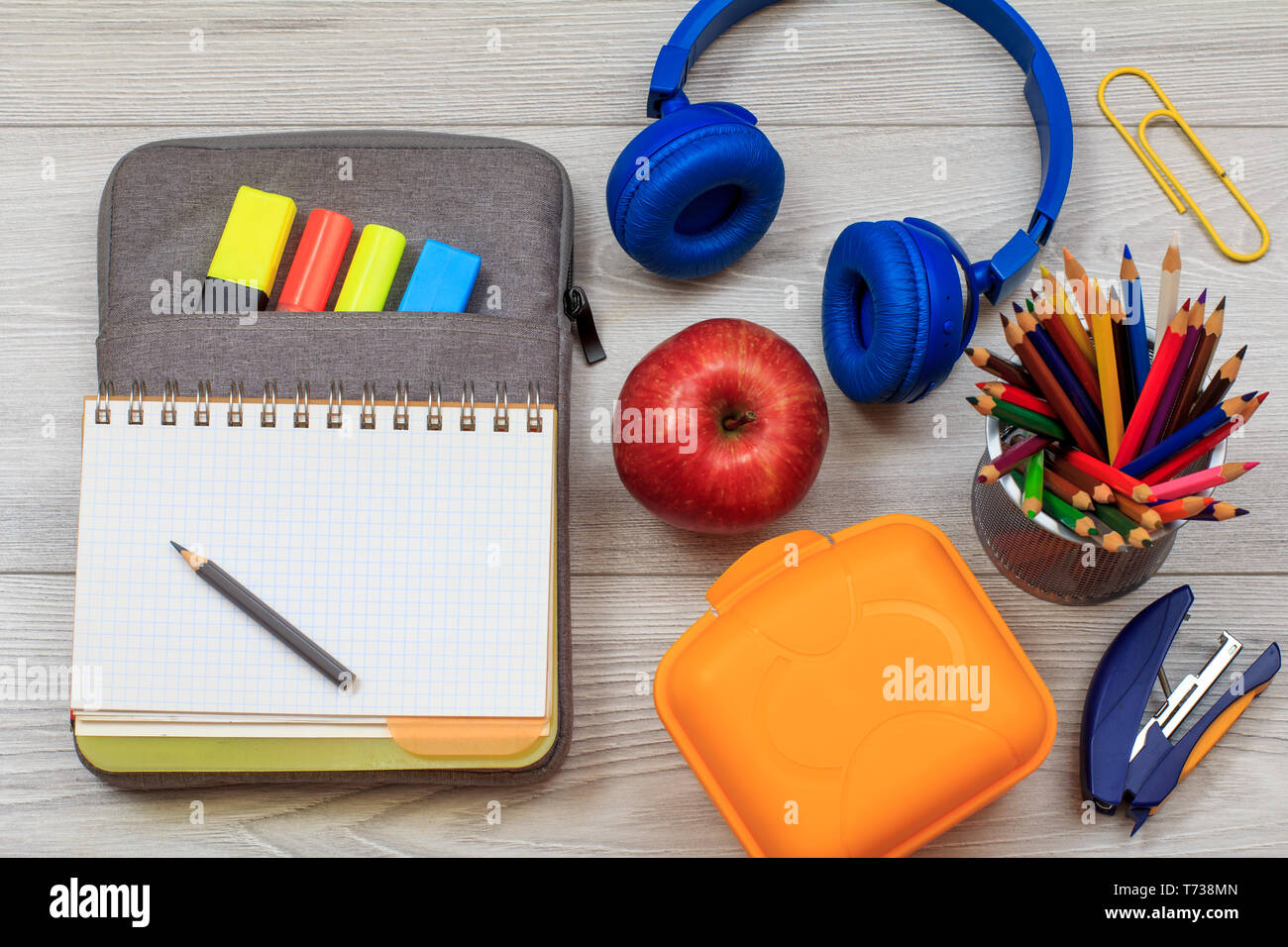 Aprire il quaderno sul sacchetto custodia a matita con colore pennarelli e  marker, scatola di pranzo, Apple, matite colorate, cucitrice e cuffie su  grigio di tavole di legno Foto stock - Alamy