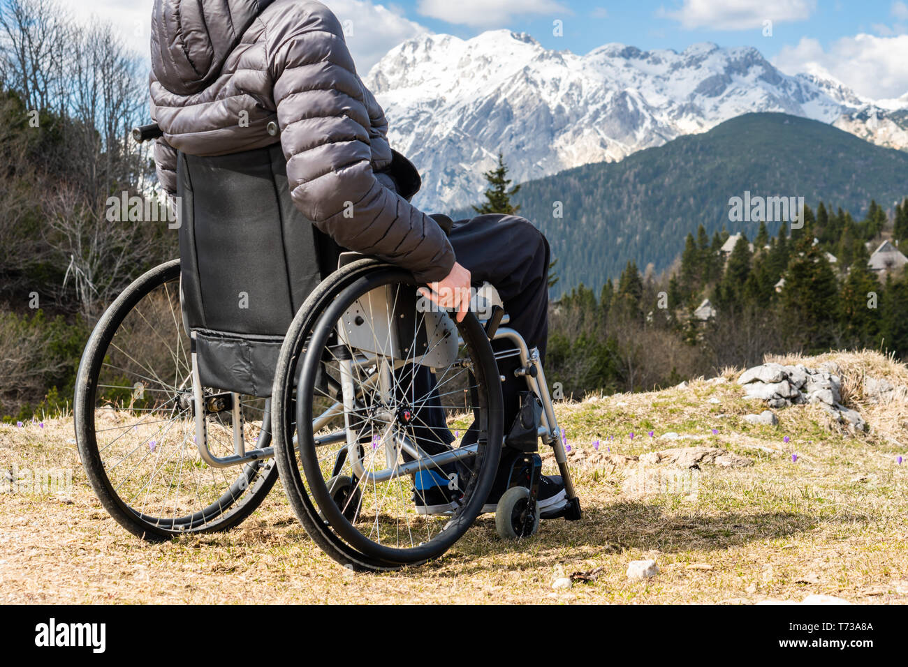 Primo piano del giovane uomo disabili su sedia a rotelle di contenimento esterno in natura osservando le montagne e natura Foto Stock
