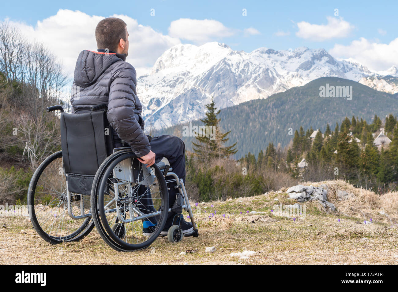 Giovane uomo disabili in carrozzella fuori in natura osservando le montagne e natura Foto Stock