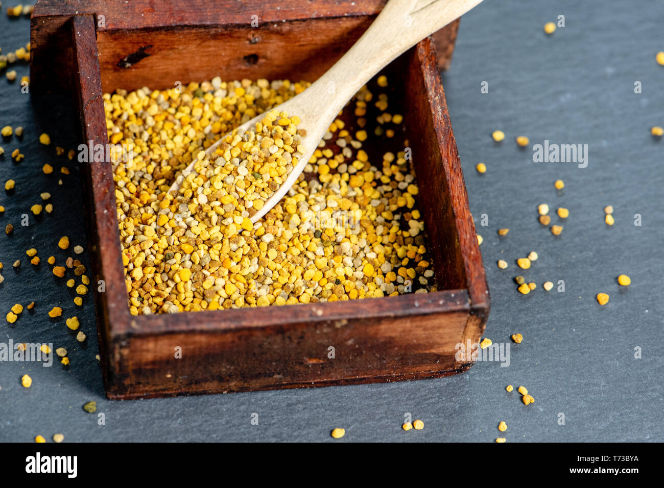 Close-up di api di granuli di polline all'interno di una piccola scatola di legno, sfondo ardesia Foto Stock