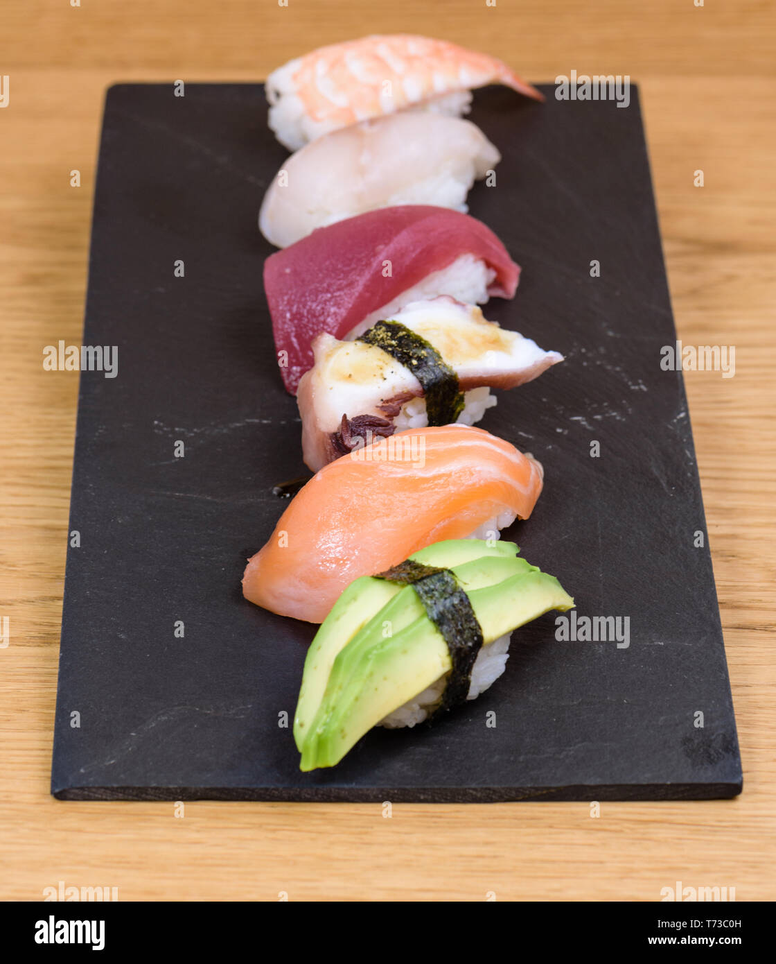 Mix di nigiri, avocado, salmone, polpo, tonno rosso, spigola, gamberi su una piastra di ardesia Foto Stock