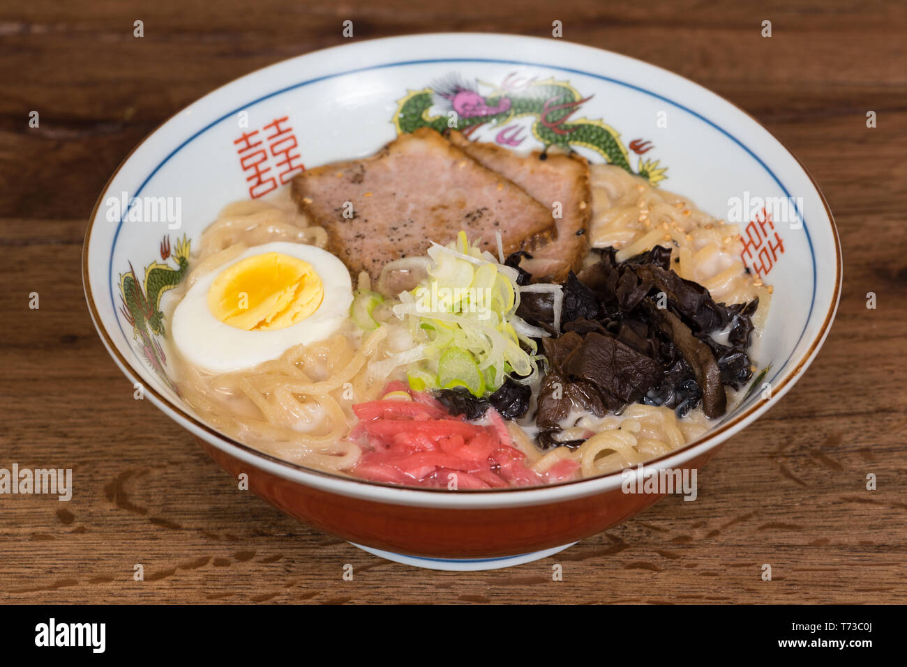 Ramen tonkotsu con carne di maiale, latte di soia, brodo di carne di maiale, funghi neri, uova, cipolle, servita in una ciotola di legno scuro dello sfondo della tabella Foto Stock